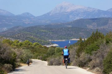 Cyklist på vej ned ad bakke i smukt landskab på øen Poros i Kykladerne
