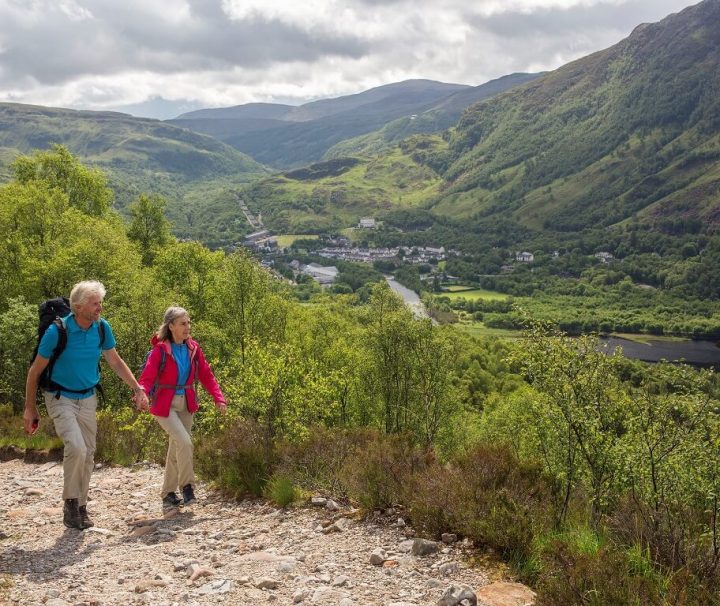 Vandrere på vej ad sti med udsigt over grøn dal i Kinlochleven. Vandreferie Skotland